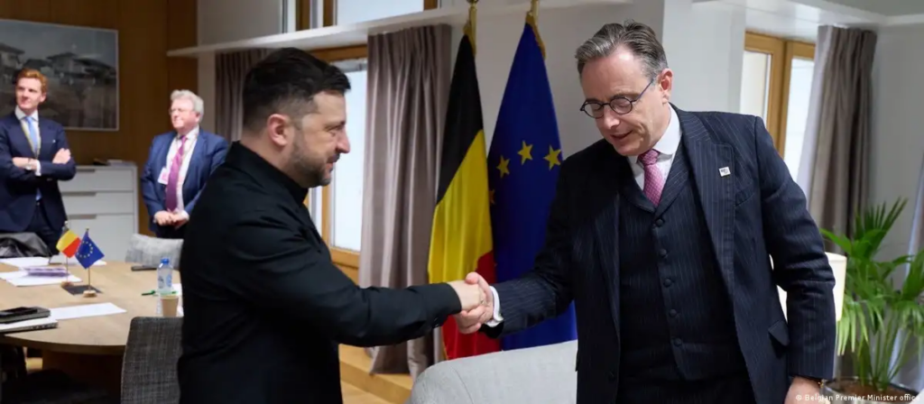El presidente de Ucrania, Volodímir Zelenski (izq.) y el primer ministro belga, Bart De Weber, se saludan en Bruselas previo a la reunión entre representantes de los 27 países de la Unión Europea el viernes (19.12.2025) Foto: Belgian Premier Minister office vía dw